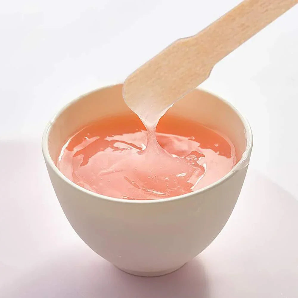 Un bâton en bois applique un produit liquide rose dans un bol blanc pour une épilation naturelle.