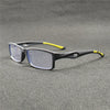 Un par de gafas deportivas anti-luz azul gris oscuro con detalles amarillos, apoyadas sobre una superficie gris oscura.