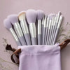 A collection of 22 professional makeup brushes with synthetic bristles standing upright in a lavender fabric holder.