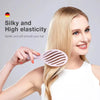 A woman is using a pink hollow-out detangling hair brush on her blonde hair.
