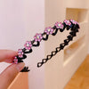 A hand holds a black rhinestone wave headband with pink flowers against a white background.