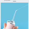 A hand holds a pink portable oral irrigator device with a thin water stream directed towards the viewer.