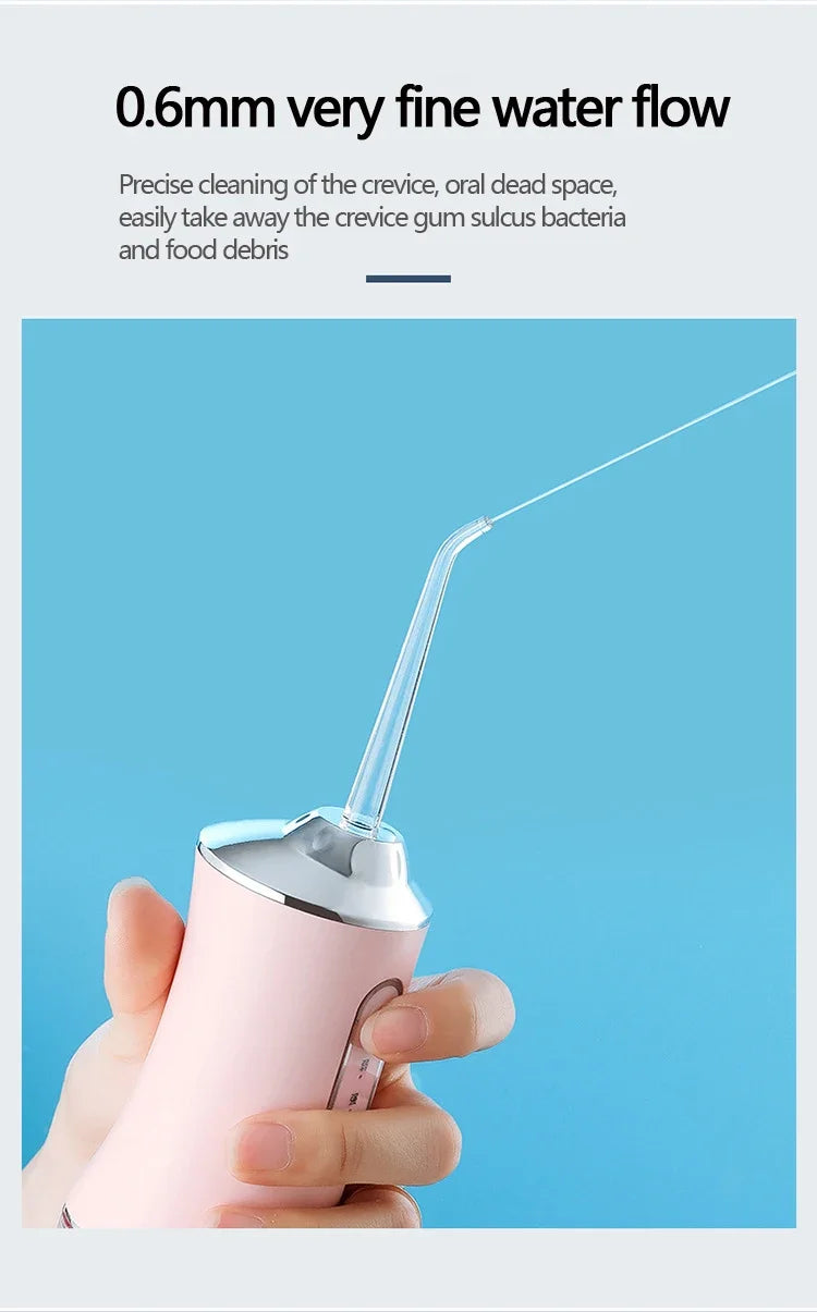 A hand holds a pink portable oral irrigator device with a thin water stream directed towards the viewer.