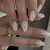 Close-up of a hand displaying reusable press-on nails with a white base and black polka dots on an almond shape.