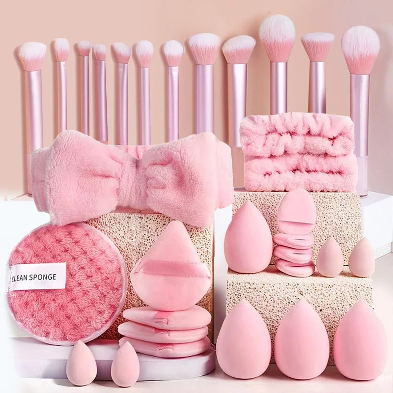 A collection of pink makeup tools including brushes, puffs, and sponges arranged on a white surface.