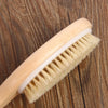 A light wooden body brush with natural bristles is shown angled on a dark wood surface.