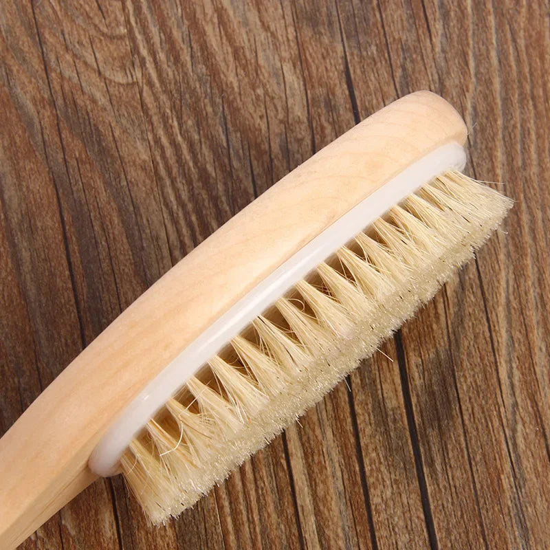A light wooden body brush with natural bristles is shown angled on a dark wood surface.