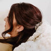 A close-up shot of a woman with dark hair wearing oval flat hair clips, resting against a fluffy white fabric.