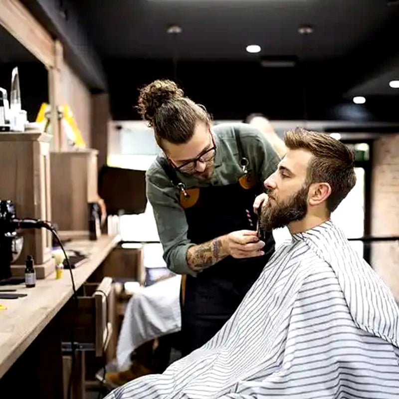 Ein Mann benutzt ein professionelles Haartrimmer-Set auf seinem Bart in einem schwach beleuchteten Salon.