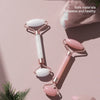 A set of resin facial massage rollers in white and pink resting on a light pink surface.