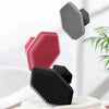 Three silicone facial cleaning and massage brushes in pink, gray, and black resting on a white towel.