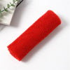 A bright red reusable exfoliating bath sponge washcloth rolled up on a white surface.