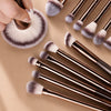 Un juego de brochas de maquillaje profesionales de doble extremo con cerdas plateadas y marrones sobre una superficie beige.