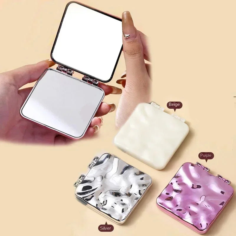 Une collection de miroirs de maquillage carrés pliables beige, violet et argentés avec une main.