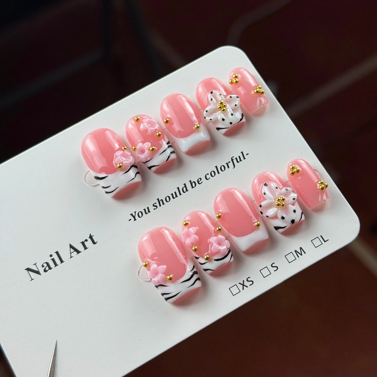 A display of hand-painted pink resin nail art designs featuring white and black stripes and gold floral accents.