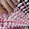 Close-up of a hand displaying pink French press shaped nails with white accents on a pink background.