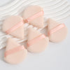 A set of three pink cosmetic powder puffs with light pink ribbon accents resting on a white striped surface.