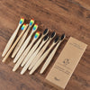 A set of ten natural bamboo toothbrushes with colorful bristles displayed on a wooden surface.
