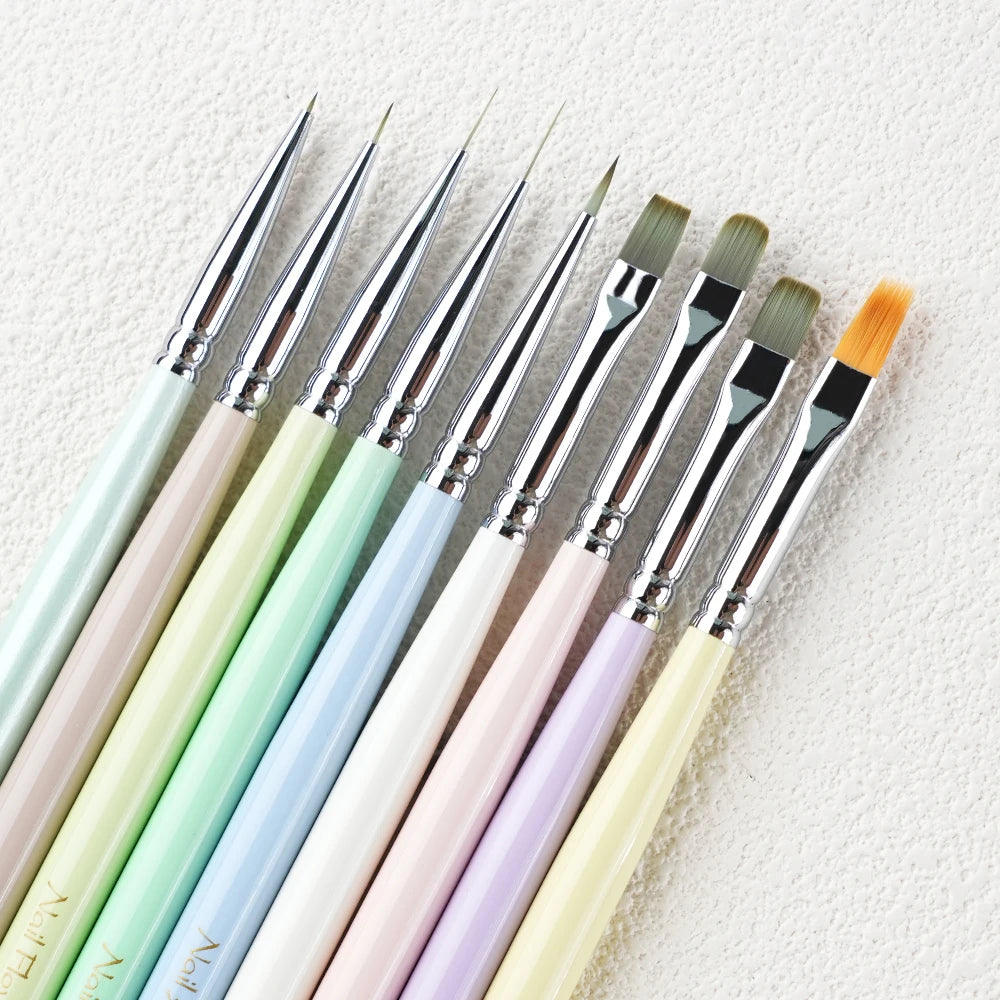 A collection of professional nail art brushes in various pastel shades laid diagonally on a white surface.