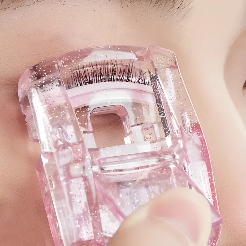 A close-up of a pink portable mini eyelash curler set being held by a finger.
