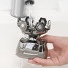 A hand holds a silver electric shaver while water flows over it.