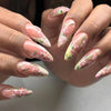 A close-up of a hand displaying press-on nails decorated with pink and green floral designs.