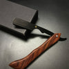Mango de madera y hoja negra de una navaja profesional de afeitado, sobre una superficie oscura.