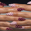 Close-up of hands displaying various red and pink striped press-on nails with an almond shape.