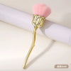 Pincel de maquillaje en forma de rosa dorado con cabeza peluda rosa sobre una superficie blanca.