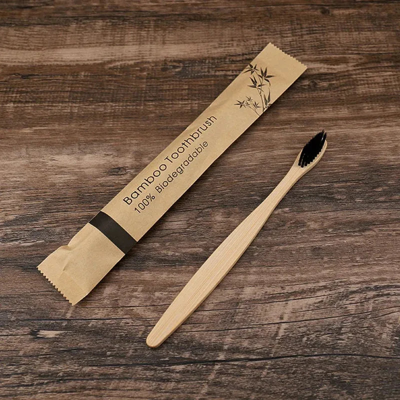 A bamboo toothbrush packaged in natural paper, lying next to the wooden brush on a dark brown surface.