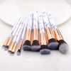 A set of ten professional makeup brushes with white and gold handles and gray bristles displayed on a white plate.
