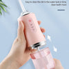 A hand holds a pink portable and detachable water tank design oral irrigator device.