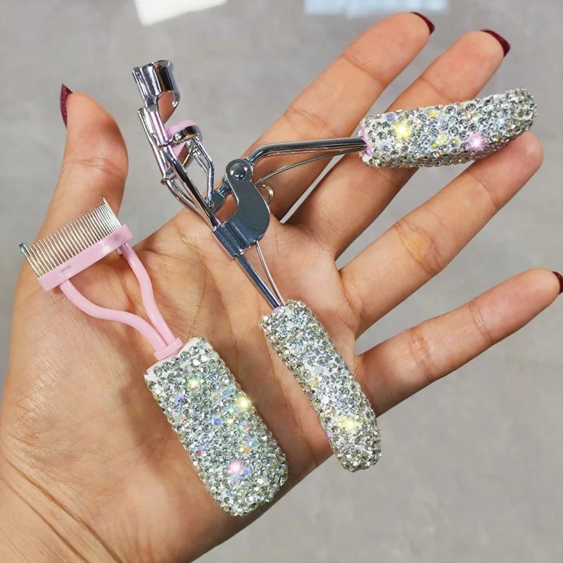 A hand holds a professional eyelash curler set with silver metal tools and glitter-covered silicone applicators.