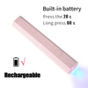 A pink portable rechargeable UV LED nail dryer with a button and light emitting from the tip.