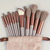 A set of thirteen professional makeup brushes with rose gold and gray handles resting on a beige towel.