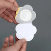 A hand is holding a disposable belly button patch, which consists of a light gray adhesive backing and a white circular pad.