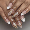 Gros plan d'une main montrant des ongles press-on français à amande roses avec des accents floraux dorés et des pointes blanc