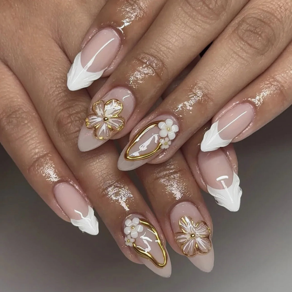 Gros plan d'une main montrant des ongles press-on français à amande roses avec des accents floraux dorés et des pointes blanc