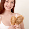 A woman holds a natural bamboo hair brush, demonstrating its use for detangling and scalp massage.