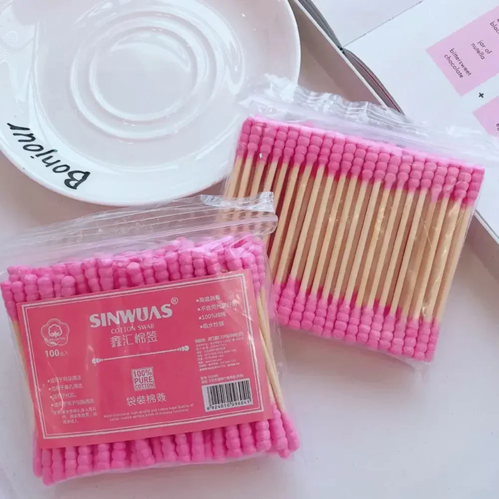 Un paquet de cotons-tiges en bambou rose et plastique clair à côté d'un plat blanc.