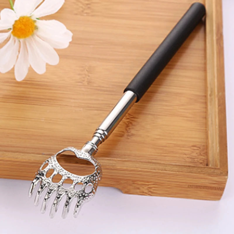 Stainless steel telescopic back scratcher with a black handle resting on a wooden board next to a white flower.