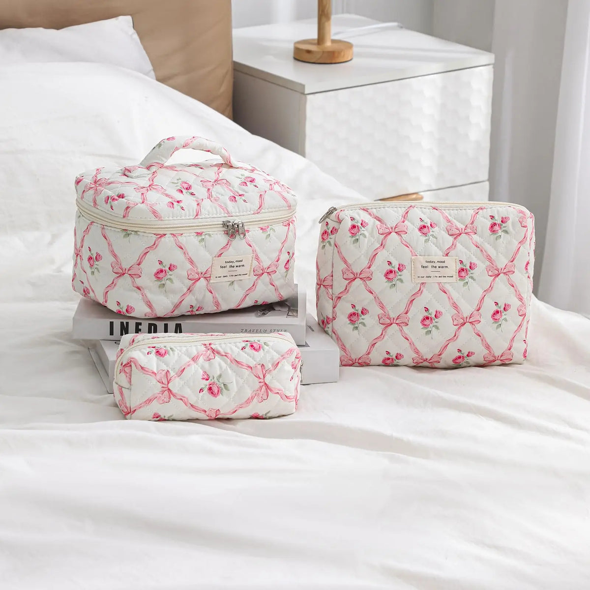 A pink and white quilted cotton makeup bag with a zipper closure resting on a white bed.