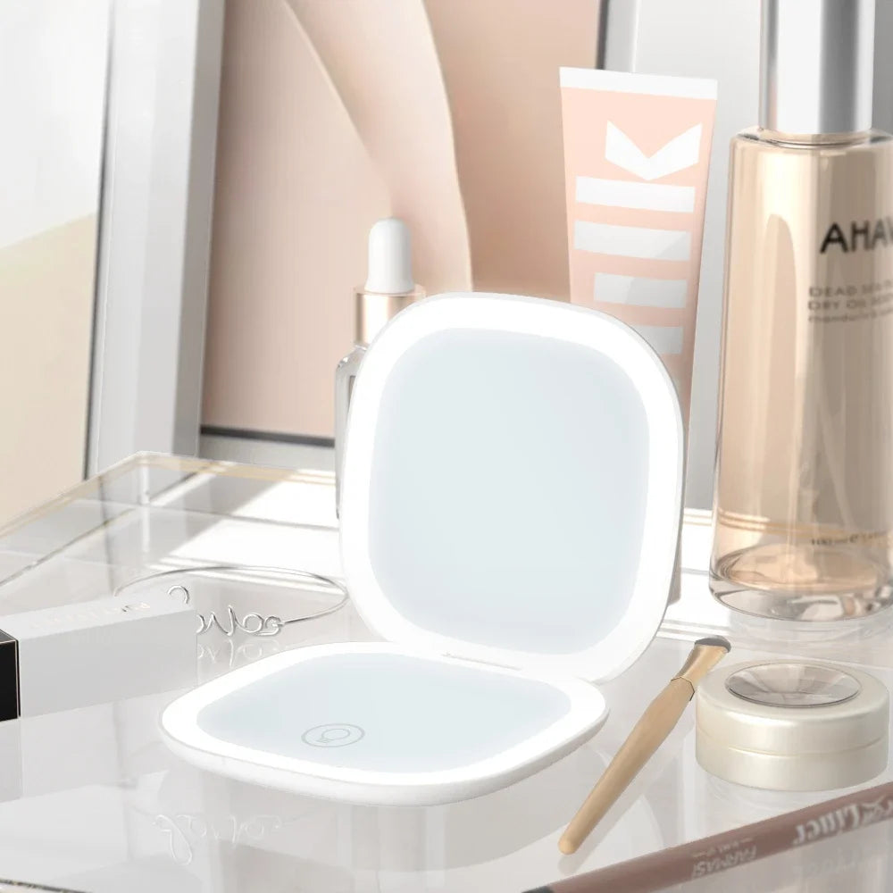 A compact LED makeup mirror with a hinged lid and a separate magnifying mirror are displayed on a glass surface.