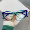A pair of blue-tinted cat eye reading glasses are held up against a white background by a person's hand.