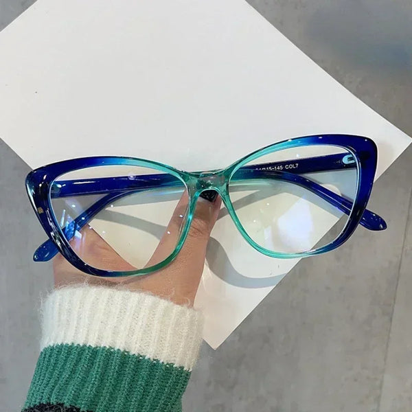 A pair of blue-tinted cat eye reading glasses are held up against a white background by a person's hand.