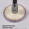 A close-up view of a large, fluffy face powder brush with a metallic handle and soft light beige bristles.
