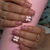 A hand displays nude pink press-on nails featuring a leopard print design and white 3D flower charms.