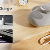 A gray electric hand massager is shown with charging cables and power banks on a wooden surface.
