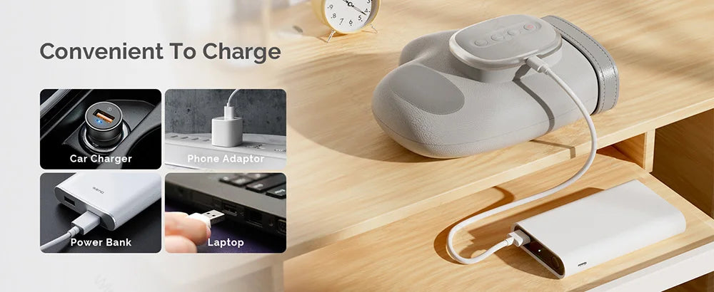 A gray electric hand massager is shown with charging cables and power banks on a wooden surface.