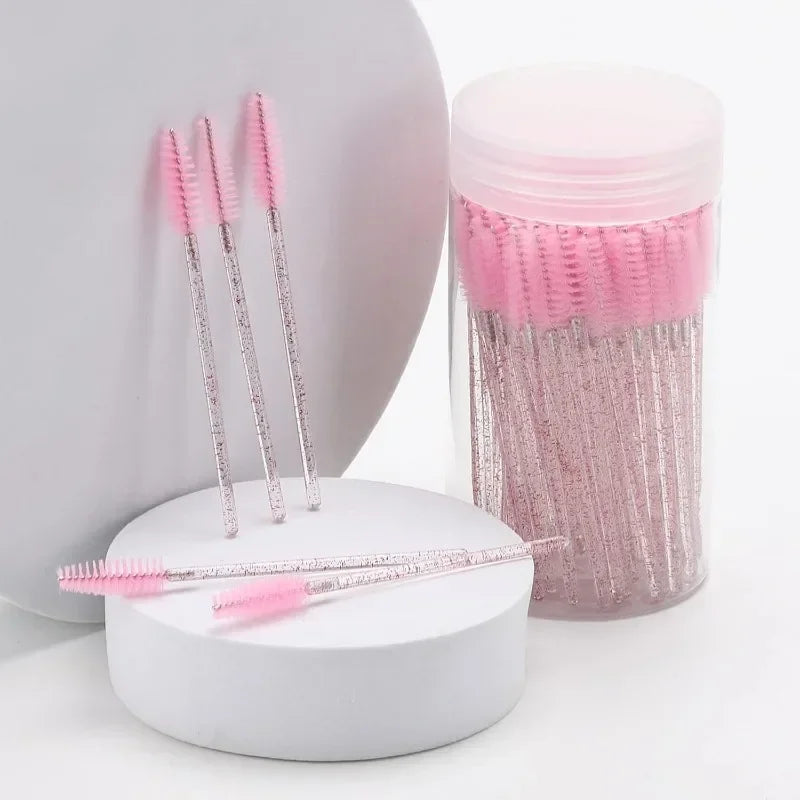 A set of pink and silver disposable eyelash and eyebrow makeup brushes displayed next to a pink cosmetic container.